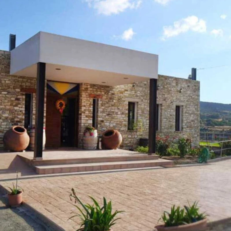 Modern stone building with a covered entrance and potted plants on a sunny day.

