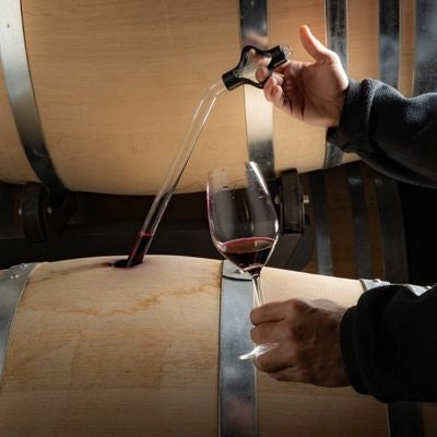 Wine being poured from a cask into a glass with a person holding the glass.